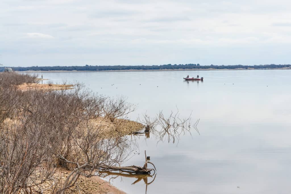 A bass boat with two anglers fishing along the shoreline of Lake Whitney near Fort Worth and Waco, Texas.