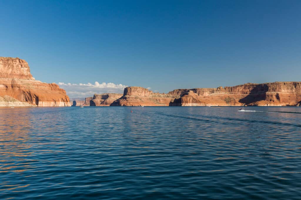 Boats motor across the blue waters of Lake Powell around the cliffs of Glen Canyon in one of the best fishing spots in Utah and Arizona.