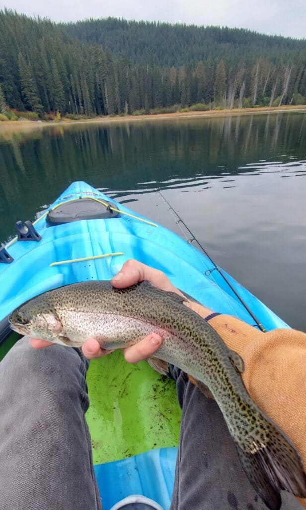 A kayak fisherman holds a trout caught in Goose Lake, Washington, an excellent fishing spot.