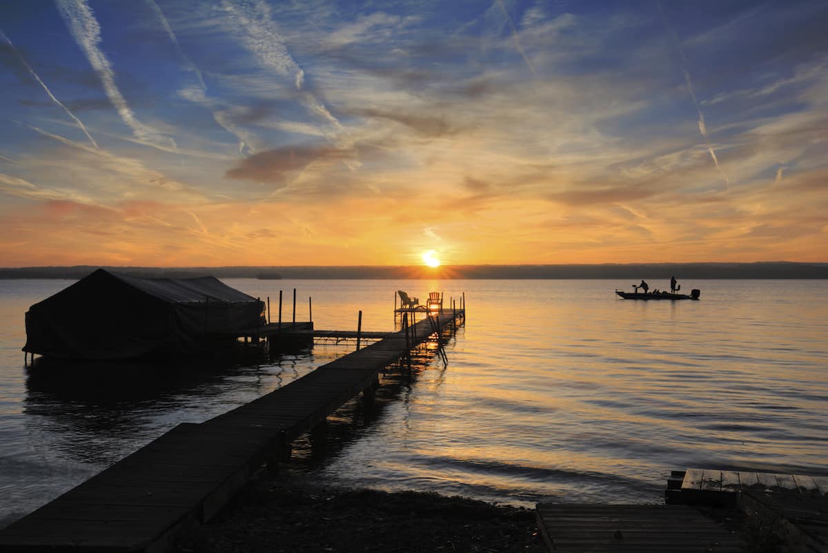 A fishing boat on the calm surface of Cayuga Lake at sunrise.