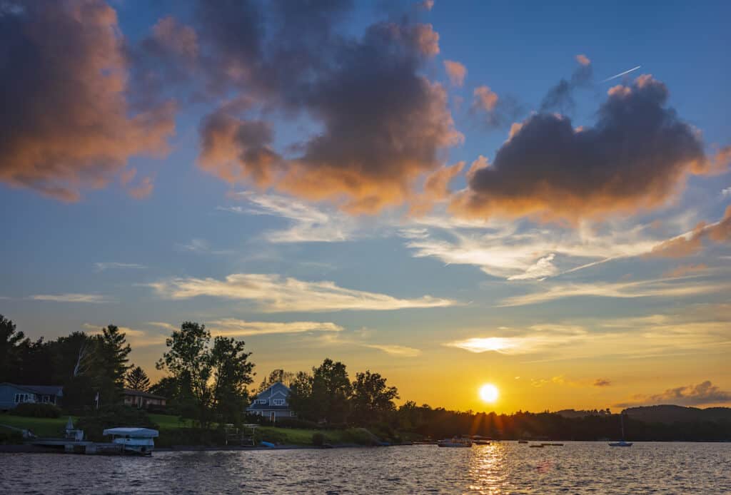 The sun sits low over Skaneateles Lake, with small fishing boats on the water.