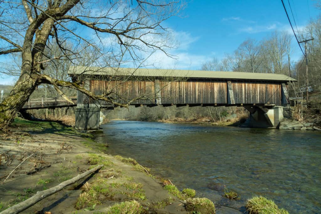 A covered bridge with the calm waters of Willowemoc Creek flowing beneath, with excellent trout habitat.