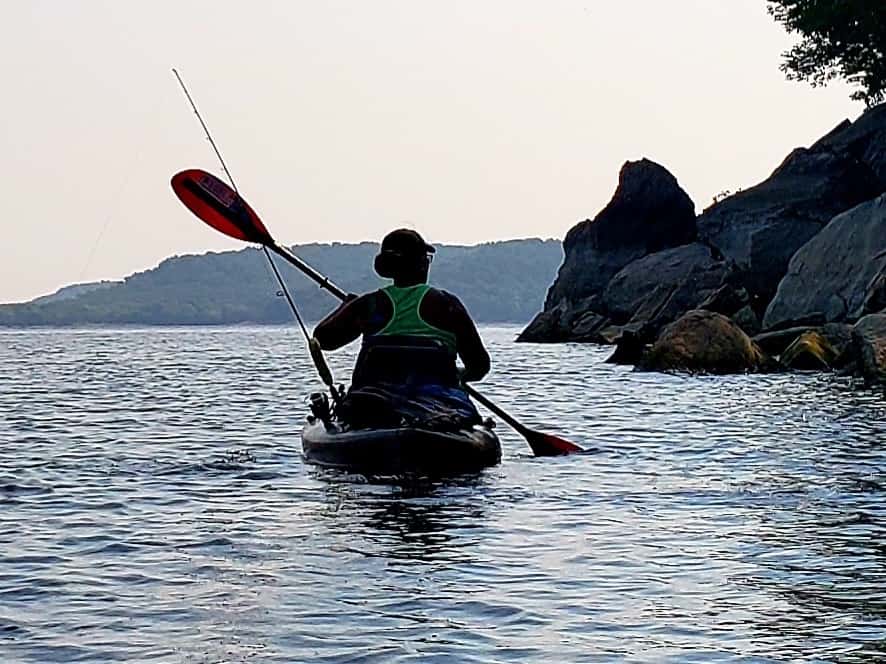 An angler kayaks with a fishing pole across Oologah Lake near sunset.