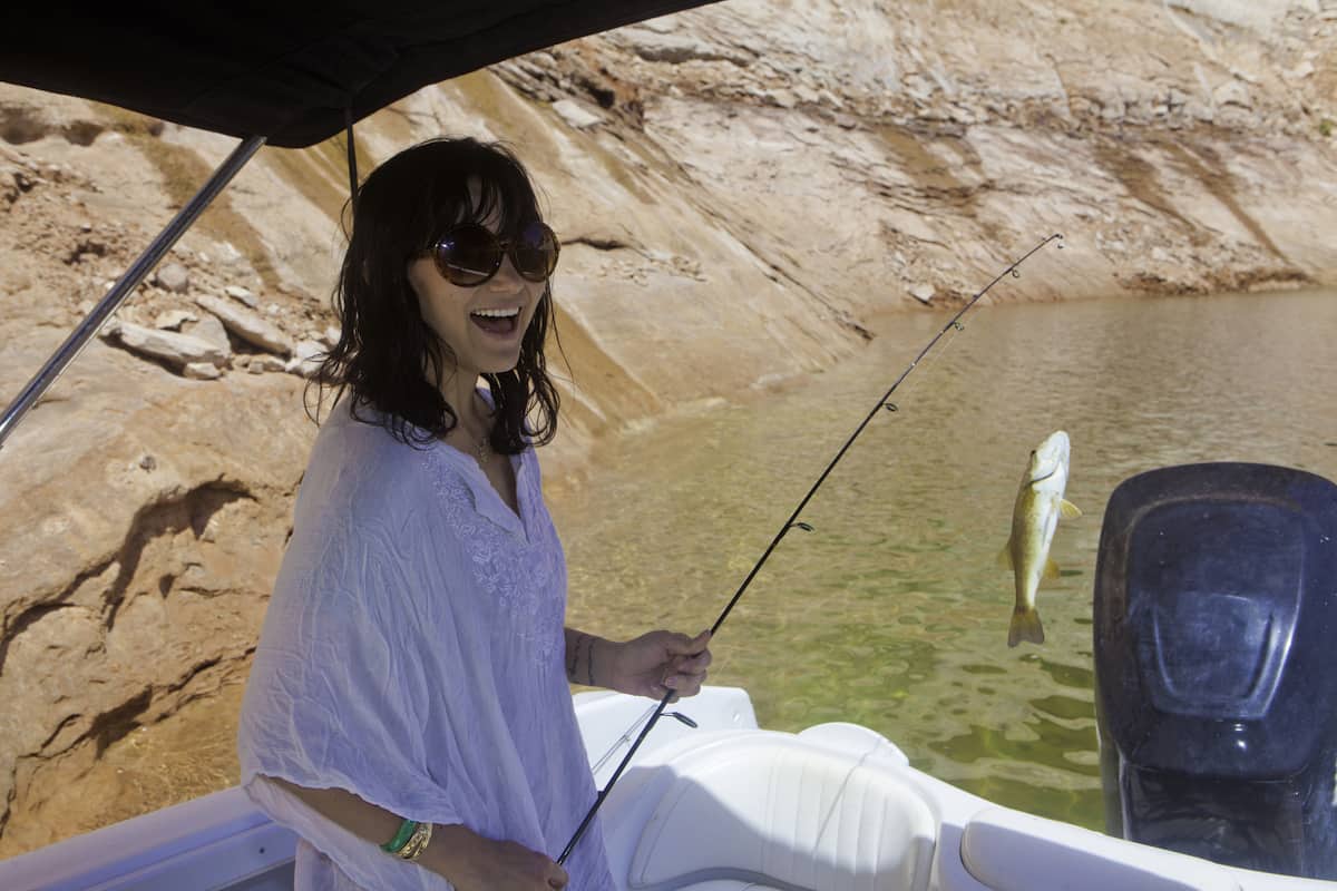 A young woman hoists a bass on the end of her line while fishing at Lake Powell.