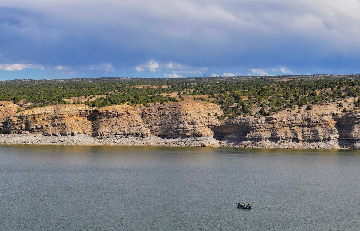 A fishing boat on the surface of Starvation Reservoir with cliffs rising in the background.