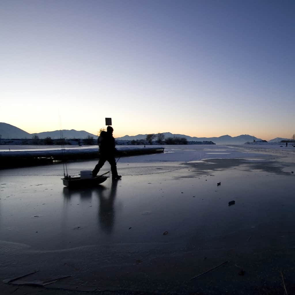 An angler pulls a sled across the ice on a frozen lake.