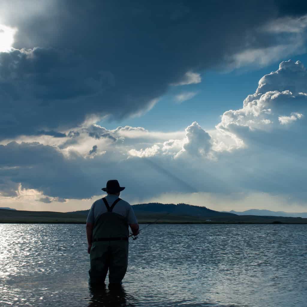 An angler in silhouette is trout fishing at dusk at Eleven Mile Reservoir in Colorado.