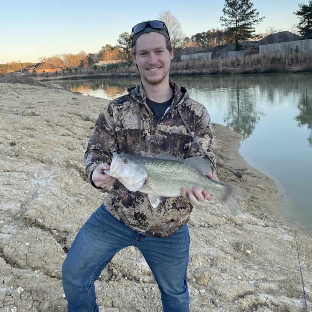 An angler holds a largemouth bass caught in Louisiana, with the water in the background.