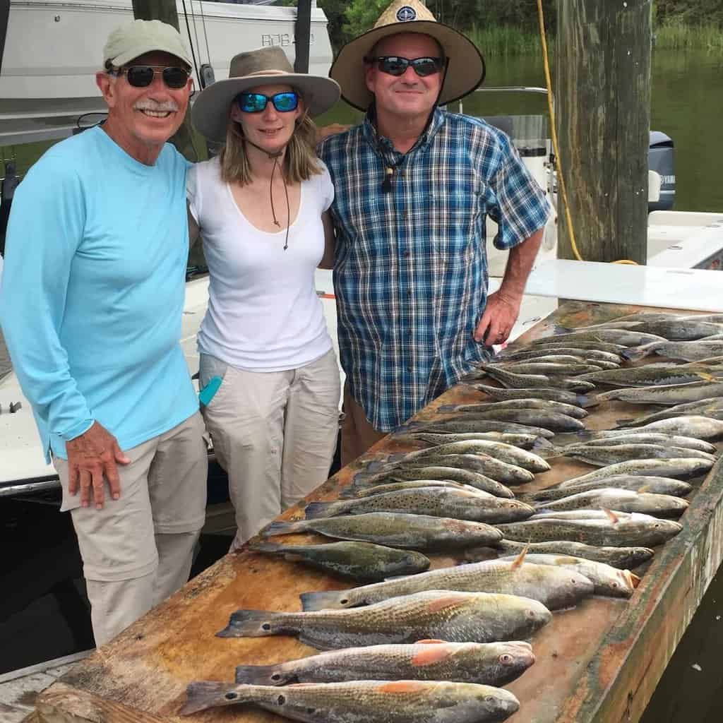 Three anglers stand next to a fish cleaning table loaded with redfish they caught fishing in Louisiana.