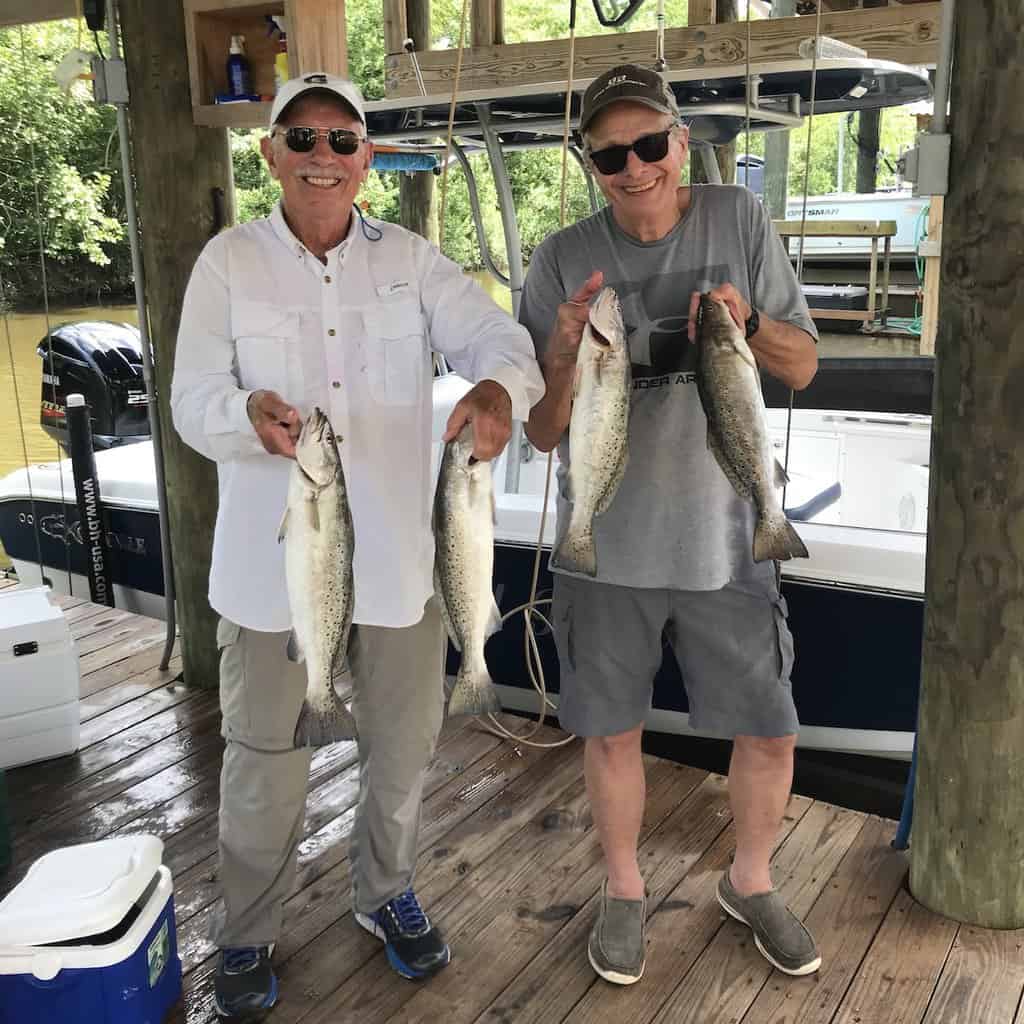 Two fishermen hold up speckled trout they caught in Louisiana.