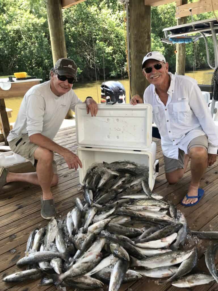 Two anglers kneel near a tip cooler spilling out a large number of speckled trout they caught fishing in Louisiana.