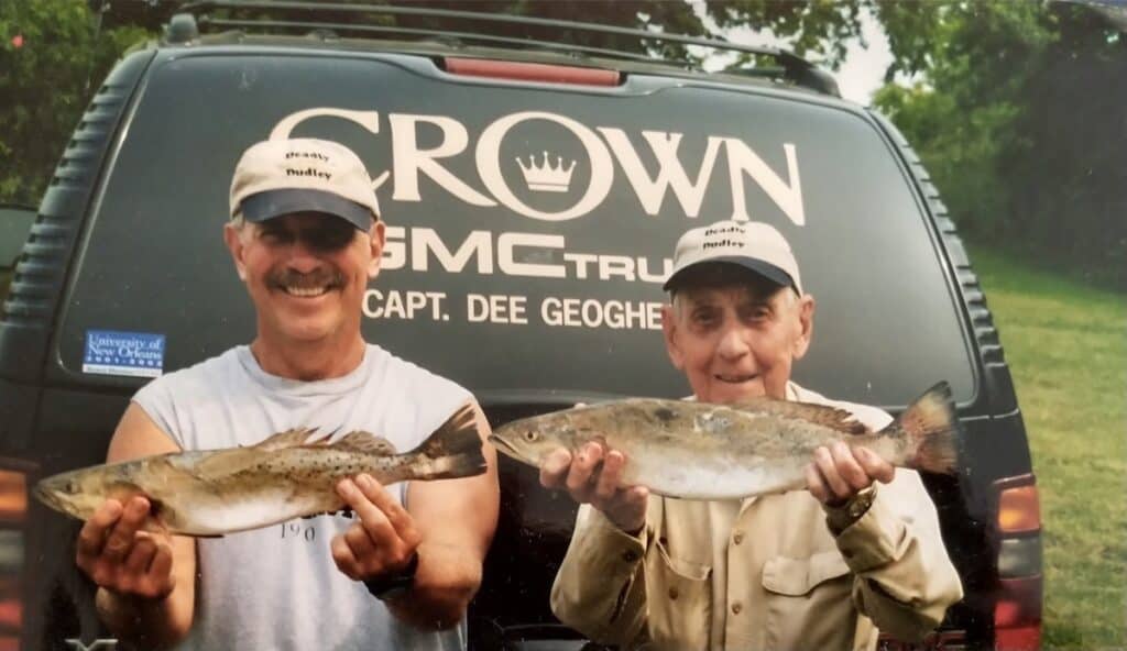 Two anglers in front of a vehicle hold up speckled trout they caught fishing in Louisiana.