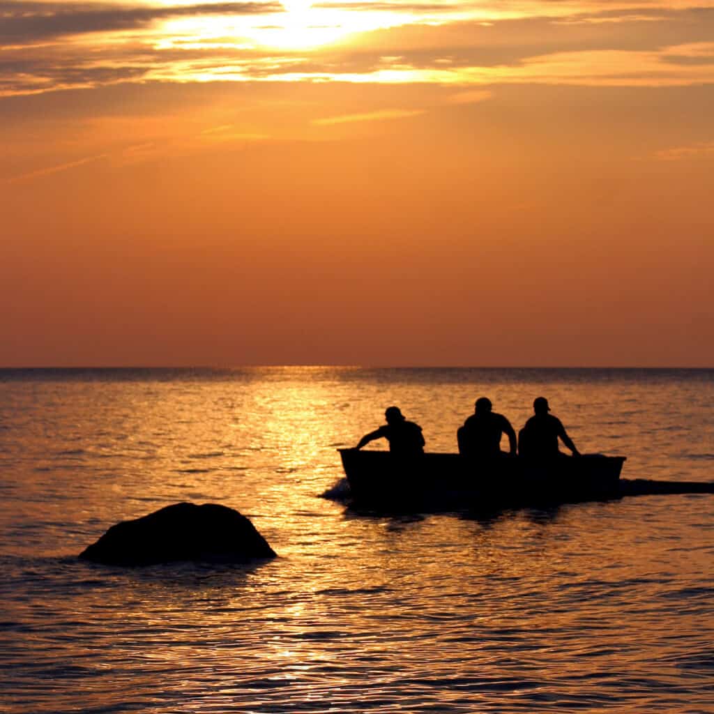 Three people fishing in a boat on Lake Erie in Ohio as the sun goes down.