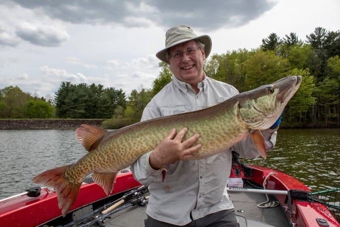 An angler holds up a massive muskellunge caught fishing in an Ohio lake in the background.
