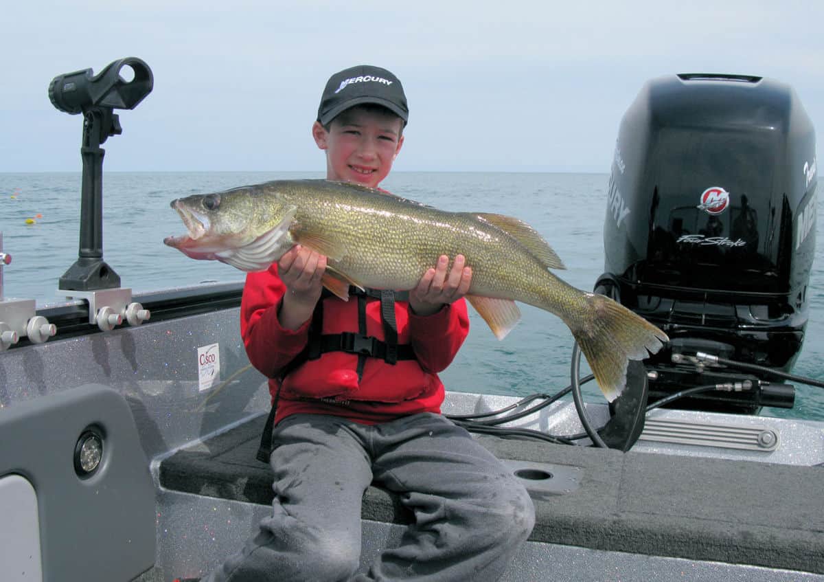 A young angler in a boat holds a large walleye he caught fishing on Lake Erie in Ohio.