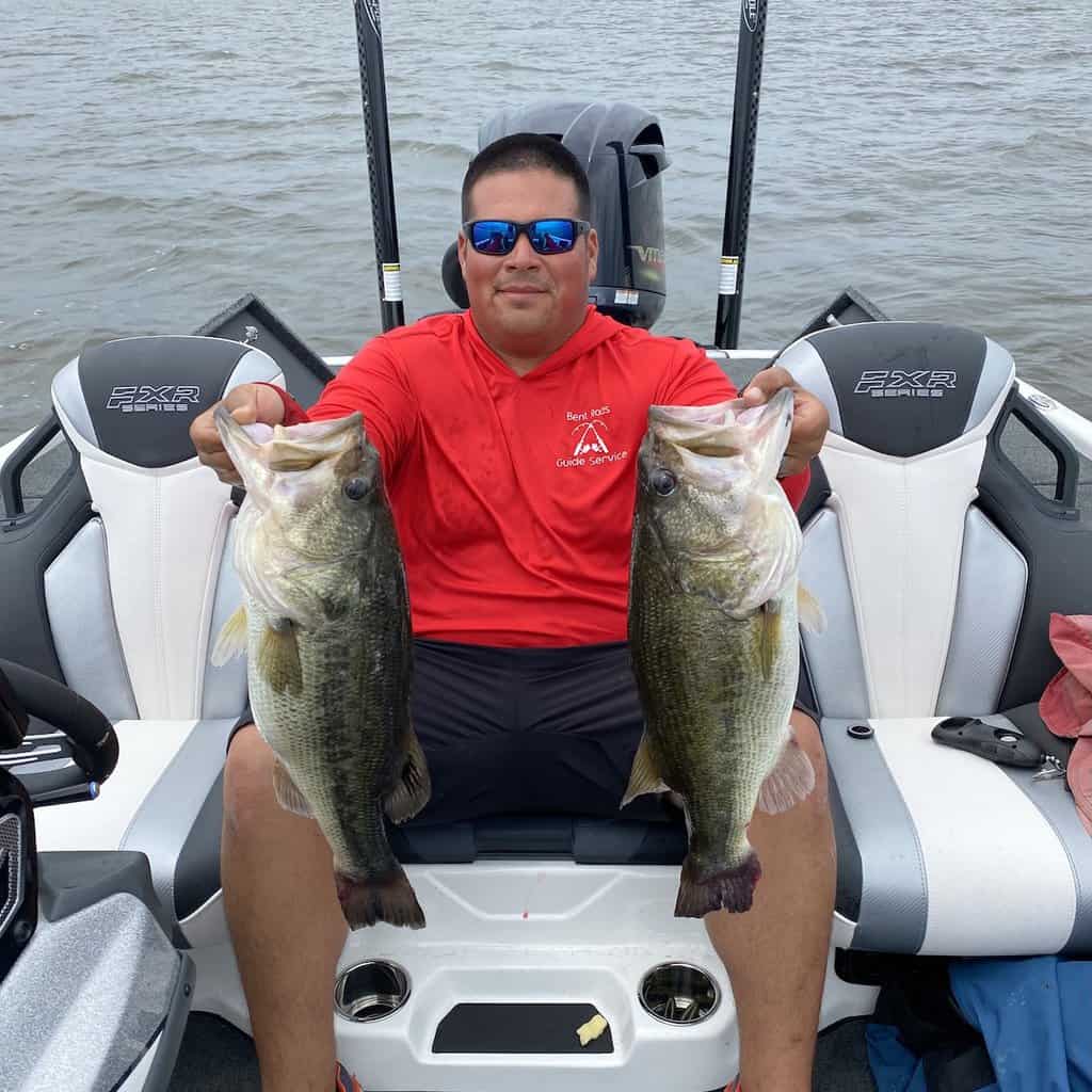 Angler wearing sunglasses in a boat holds up two giant bass he caught fishing in Toledo Bend Reservoir.