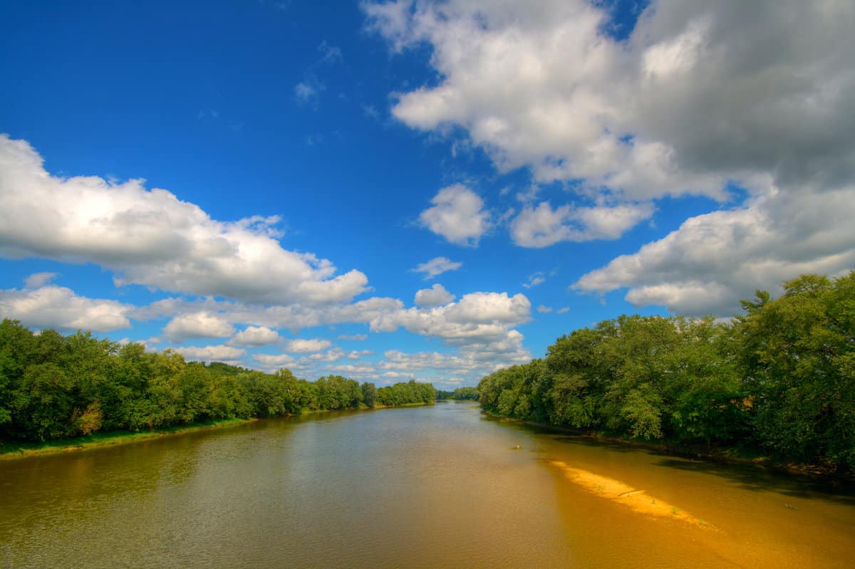 View of brown Wabash River under a blue sky with white clouds, perfect season for catfish fishing.