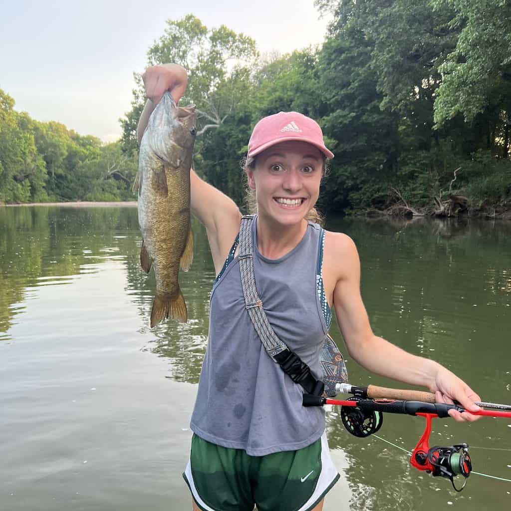 Young woman holds a smallmouth bass caught fishing and wading in Missouri.