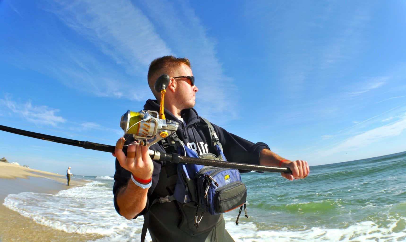 An angler holds back a large fishing rod preparing to cast into the surf while fishing for striped bass (stripers) in New Jersey.