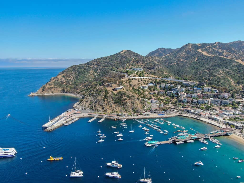 Aerial view of Avalon harbor in Santa Catalina Island with sailboats, fishing boats and yachts moored in calm bay.