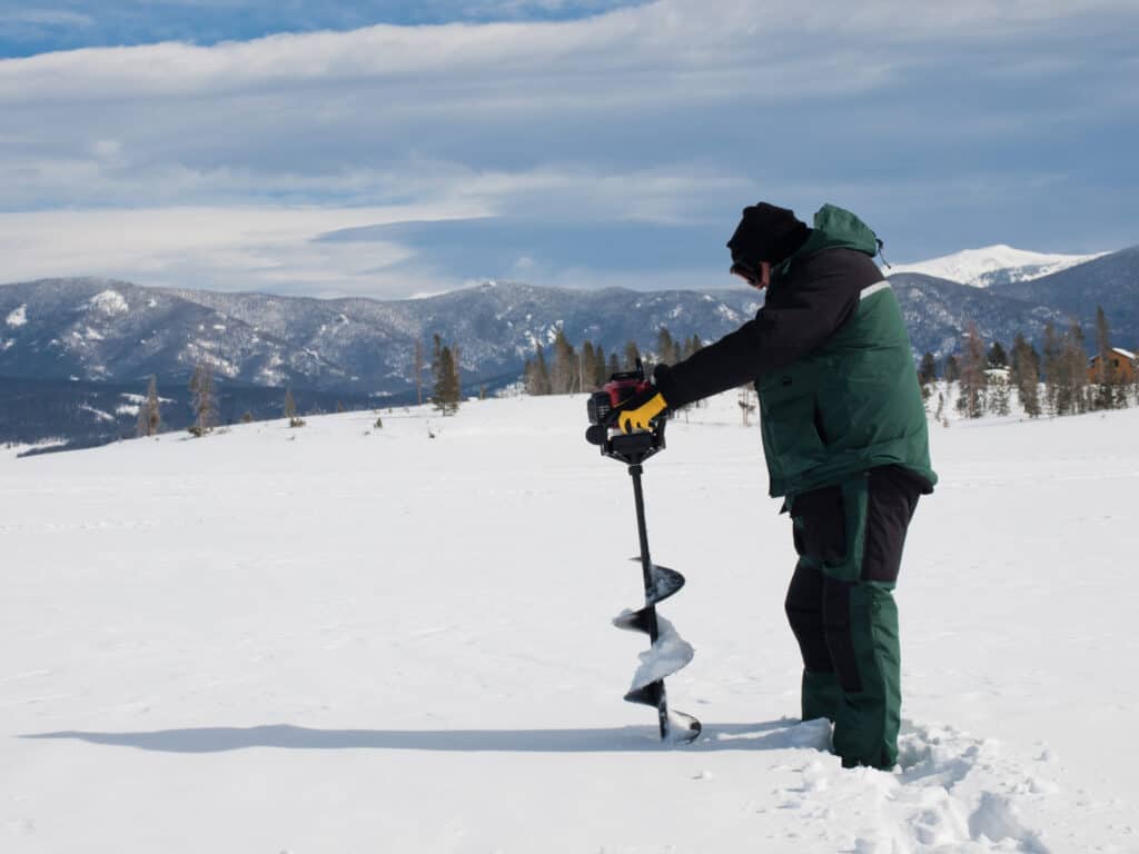 Fisherman using an auger to drill an ice fishing hole on a frozen lake Granby, Colorado.