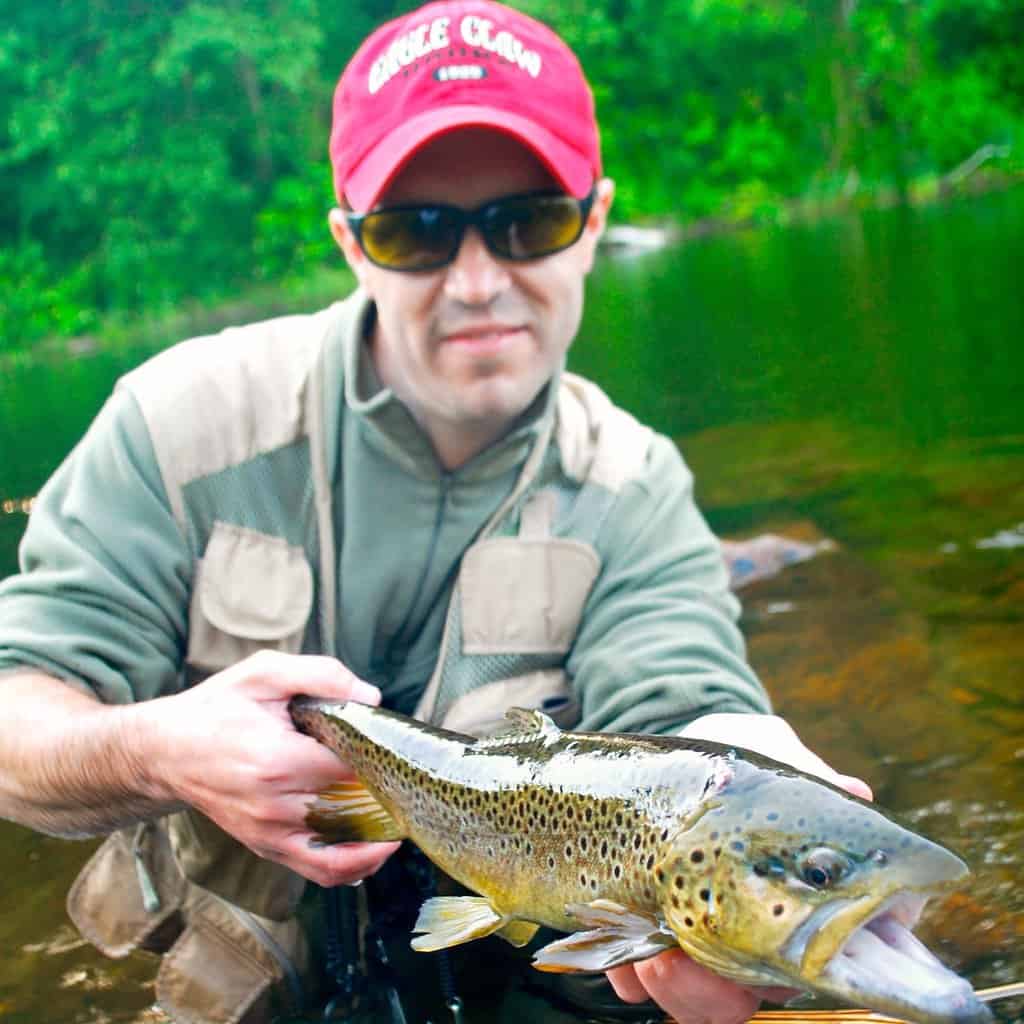 Expert fisherman Matt Wettish holds a large brown trout while wading in a Connecticut river.