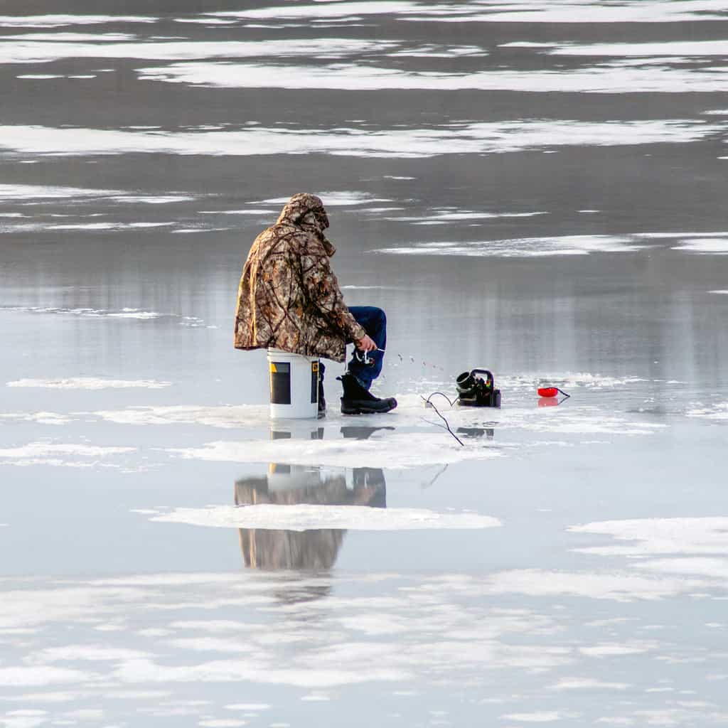 A lone angler ice fishing on a frozen lake in Michigan.