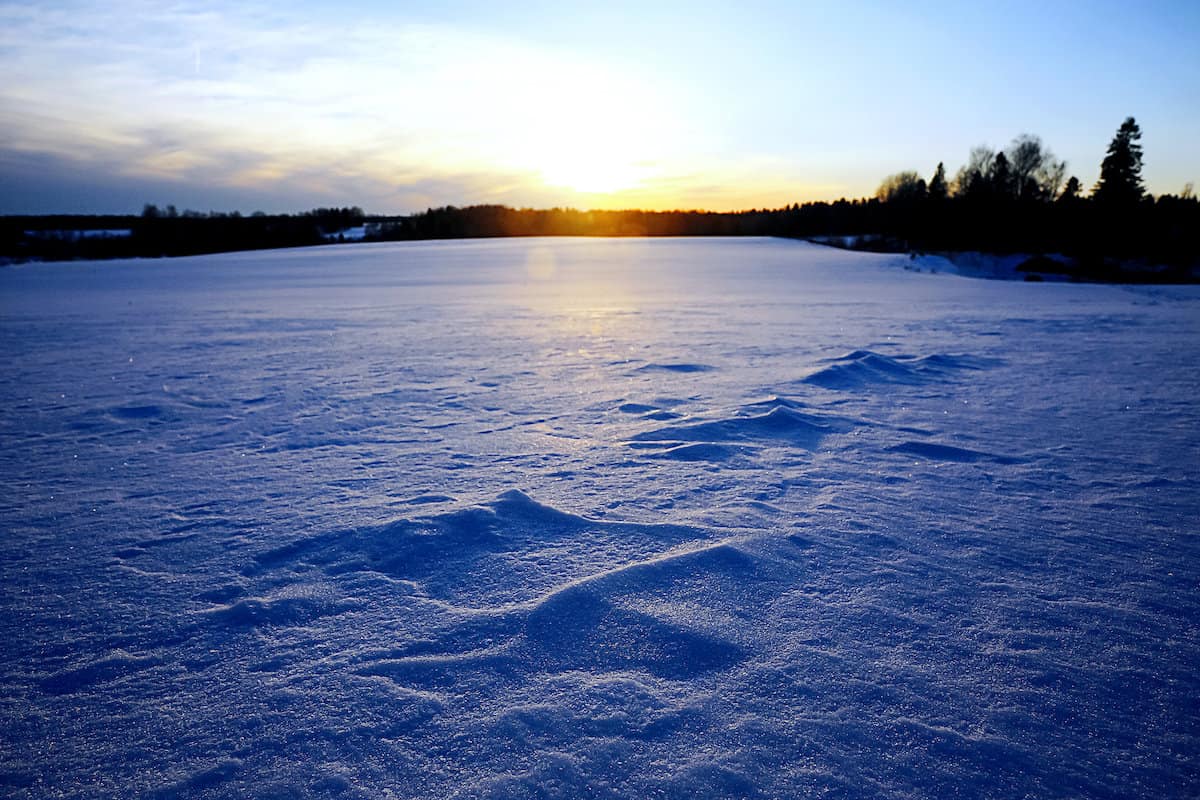 Sun peeking over the horizon beyond the surface of a small frozen lake ready for ice fishing.