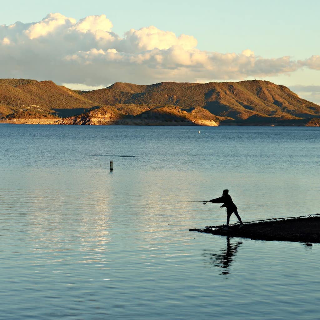A silhouette of an angler casting into Lake Pleasant, an excellent fishing spot near Phoenix.