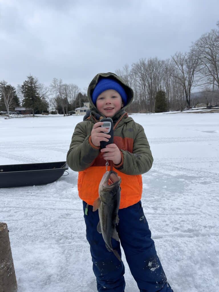A boy holds a largemouth bass on a hand-held scales during the Cheshire Fire Department's ice fishing derby.