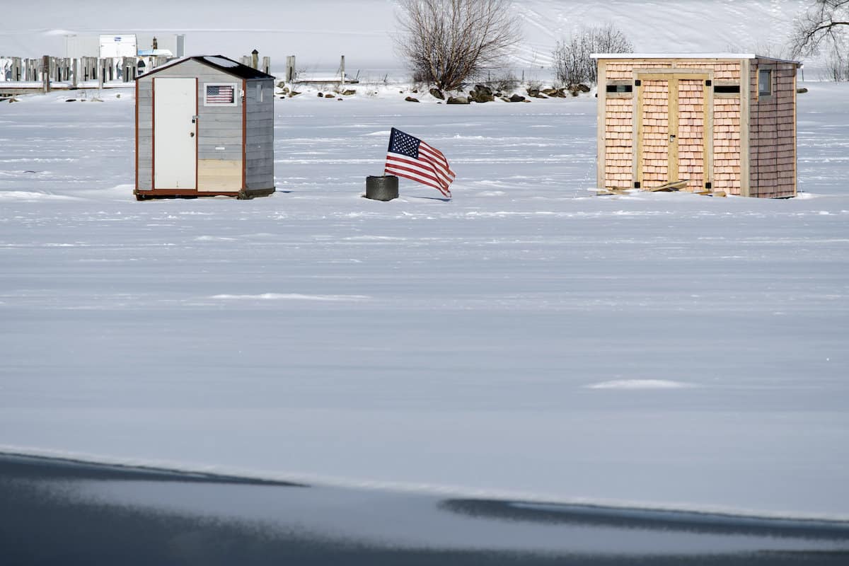 An American flag stands between two ice fishing shacks on frozen Lake Winnepesaukee, one of New Hampshire's best ice fishing lakes.