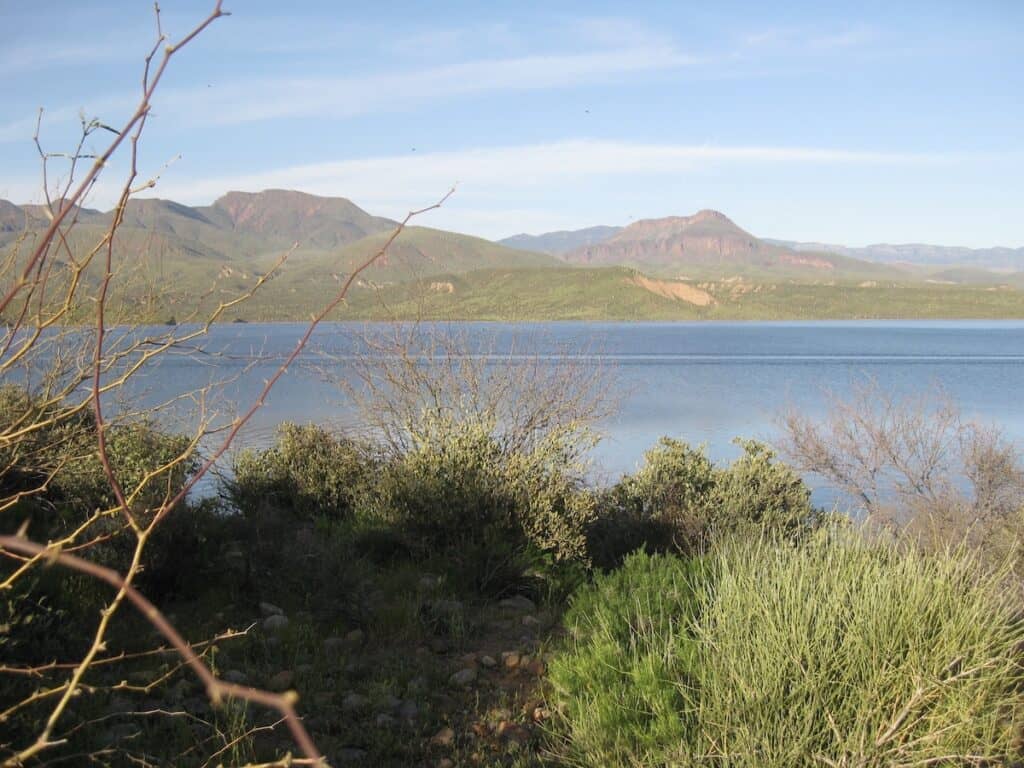 Theodore Roosevelt Lake from the shore in the desert outside of Phoenix, with green hills behind.