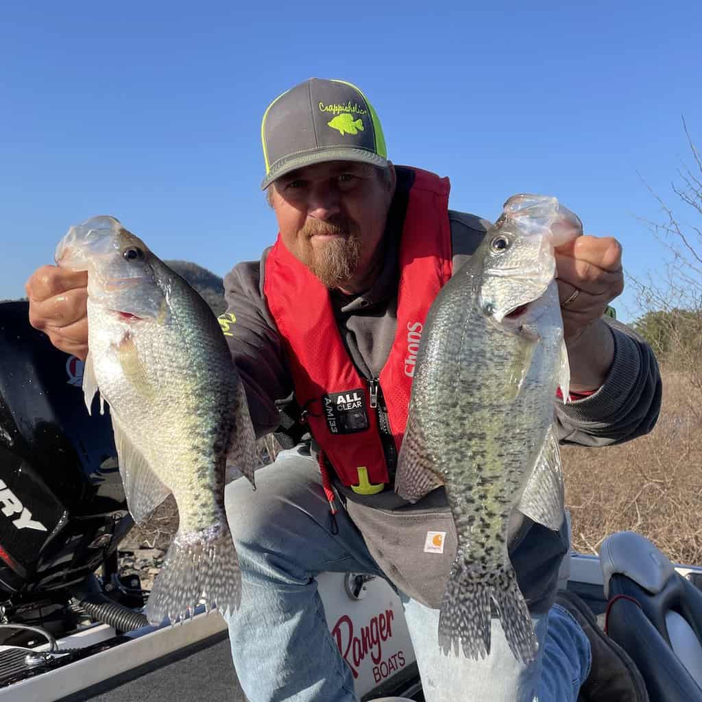 An angler on a boat holds two large crappie he caught fishing on Greers Ferry Lake in Arkansas.