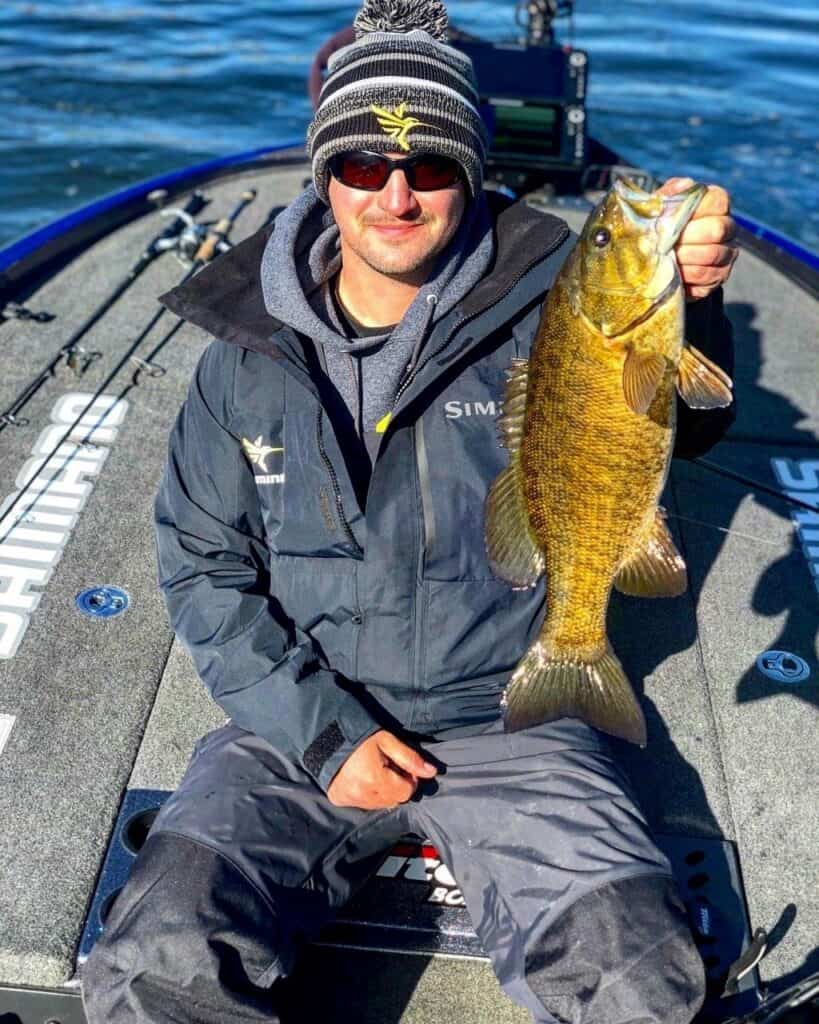 Angler in a boat holds up a single large smallmouth bass caught on Candlewood Lake, with a little blue water showing behind the boat.