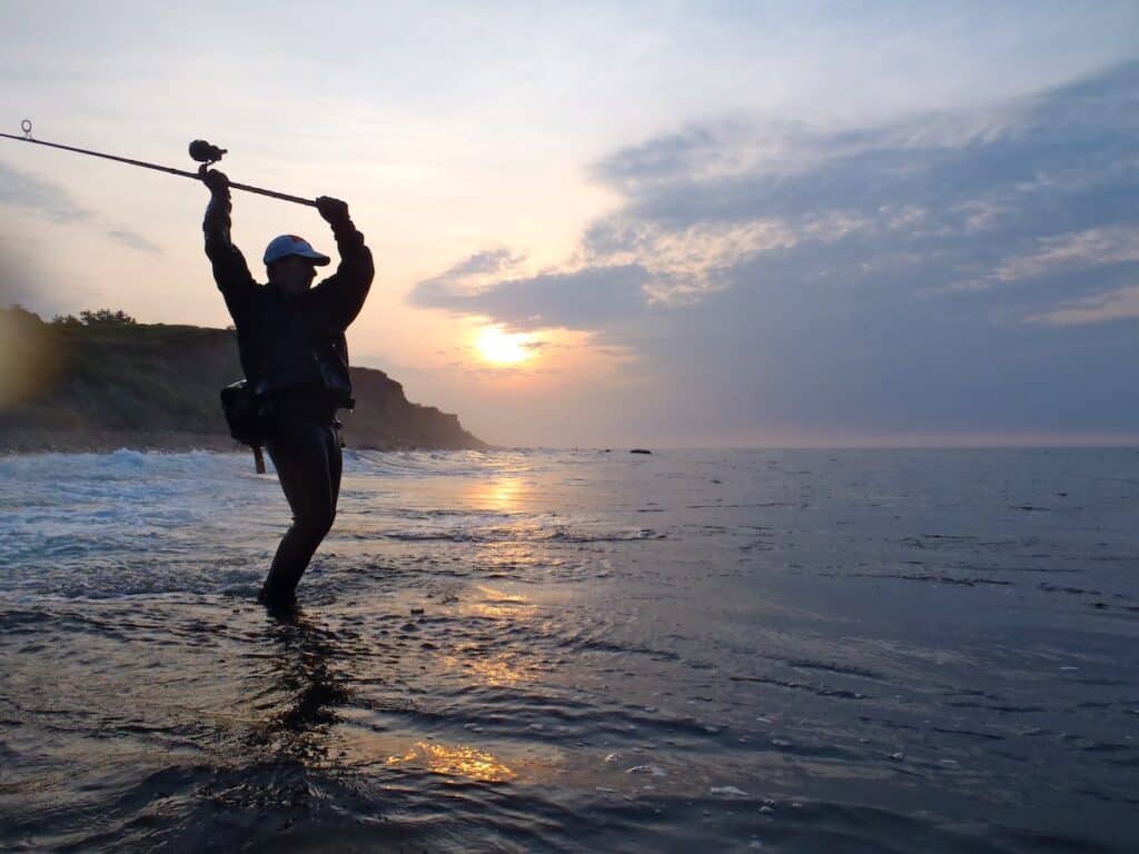 An angler in silhouette casts into the surf in Montauk, hoping to catch a striped bass.