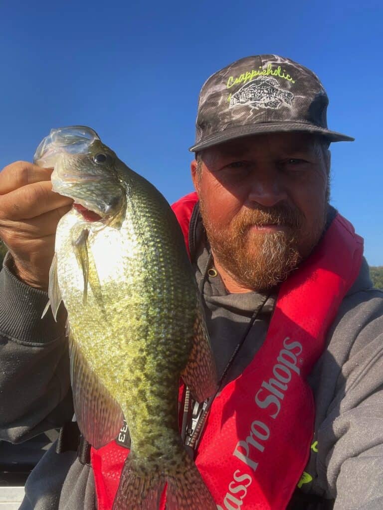 An angler in a ball cap holds a single large crappie in a selfie taken while fishing on Greers Ferry Lake in Arkansas.
