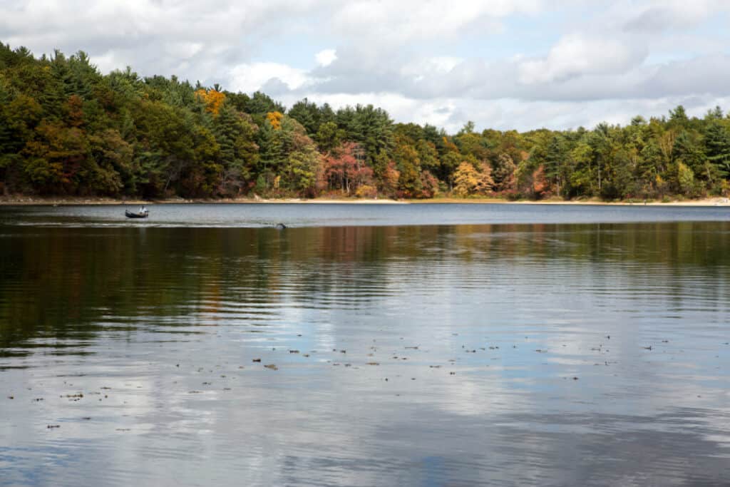 A fishing boat on the calm surface of Walden Pond in Massachusetts, with trees on the shore turning yellow and red in autumn.