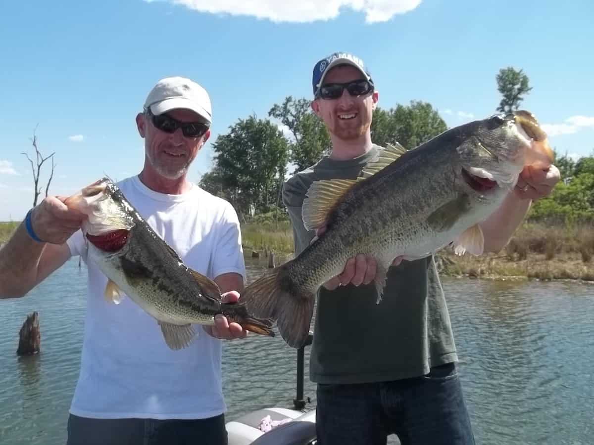 Two anglers hold up bass they caught at Texas' famous Lake Fork, which shows in the background.