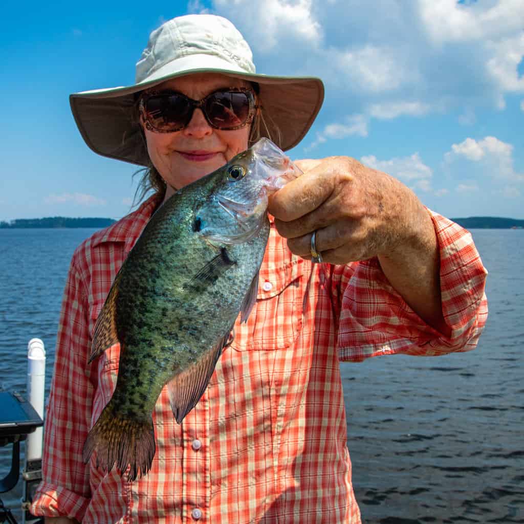 A woman in a hat holds up a large crappie caught fishing in Toledo Bend Reservoir, which is in the background.