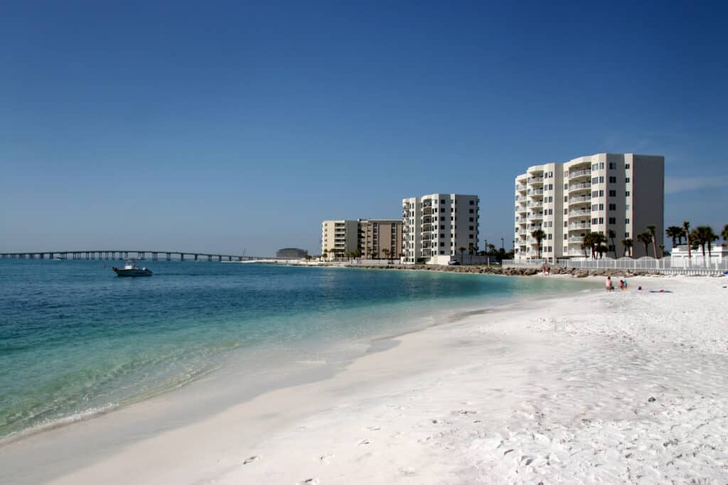 Highrise condos line the beach in Destin, Florida, with a small fishing boat traveling on blue water just off the white sand.