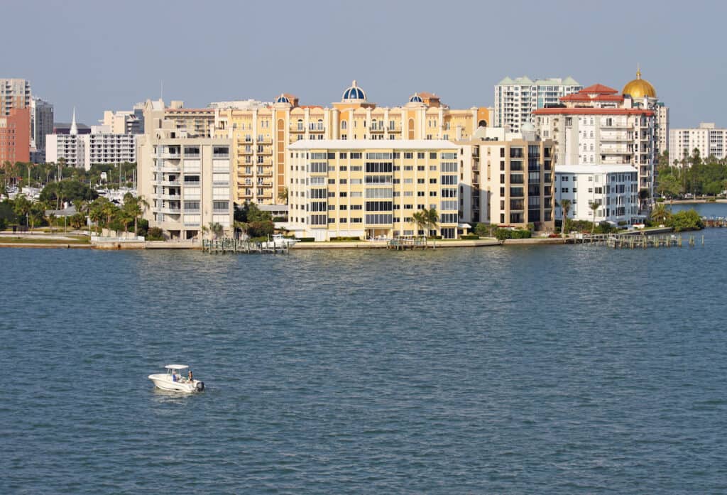 View of buildings on the edge of  Sarasota Bay, Sarasota, Florida from the water with a small fishing boat, palm trees and blue sky.
