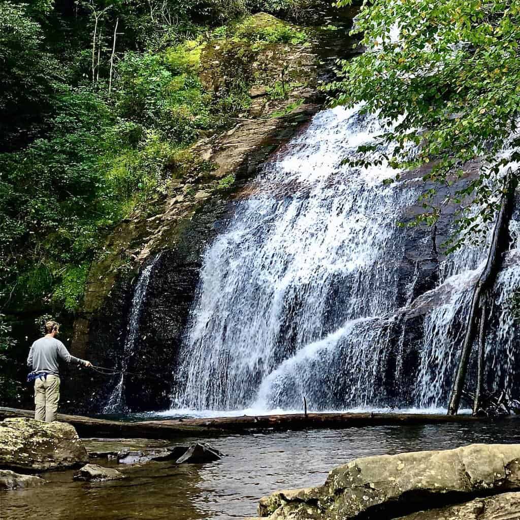 An angler fly fishing for trout in front of beautiful Helton Creek Falls in Georgia.