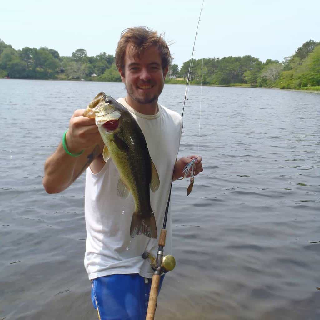 Angler holds up a nice largemouth bass caught in a Cape Cod pond behind him.