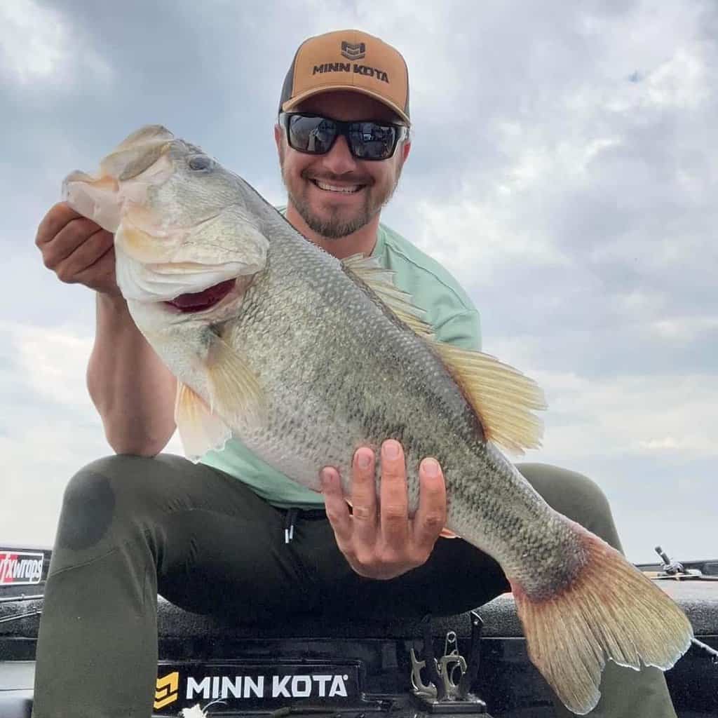 Alex Wetherell sitting on a boat holding a trophy largemouth bass he caught fishing in Connecticut.