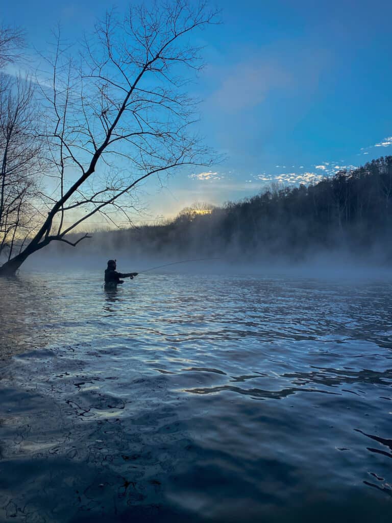 A wading trout angler in silhouette casts into the mist shrouded waters of Lake Taneycomo in Missouri.