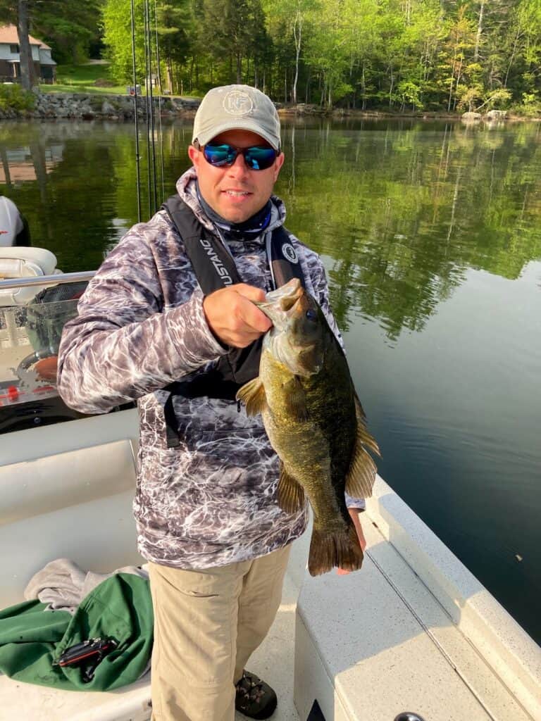 A man in a fishing boat holds a largemouth bass caught at Squam Lake, New Hampshire.