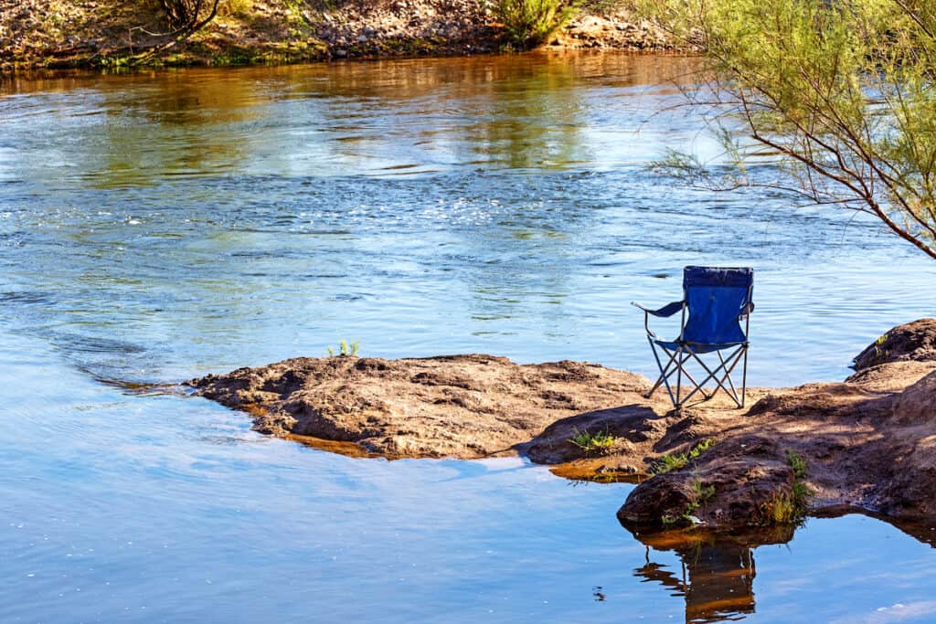 Empty chair sitting on bank of the Salt River, a popular fishing stream near Mesa, Arizona.