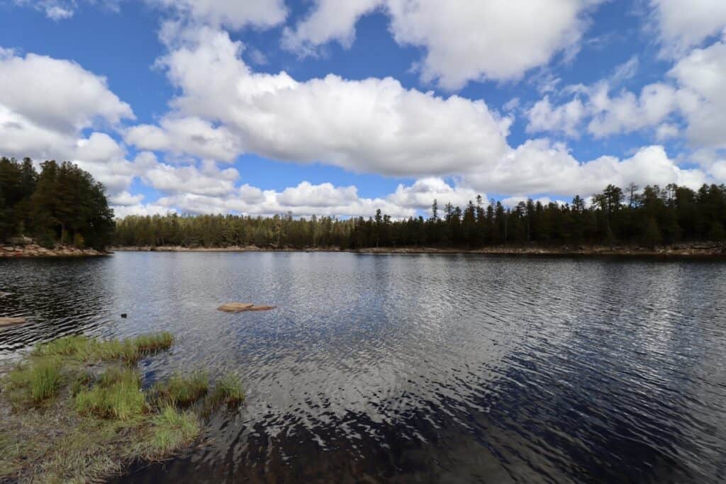 Woods Canyon Lake, a trout fishing spot along Mogollon River, reflects blue sky and white clouds.