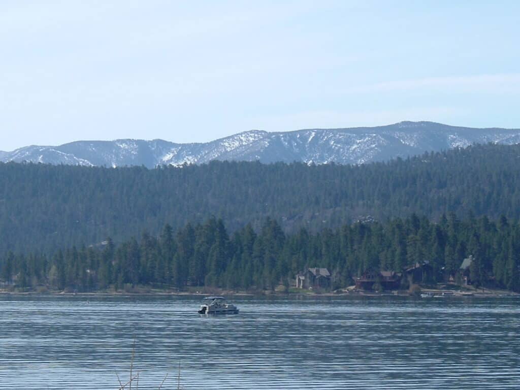 A fishing boat trolls across the surface of Big Bear Lake in the morning, with snow still on the mountains in the distance.