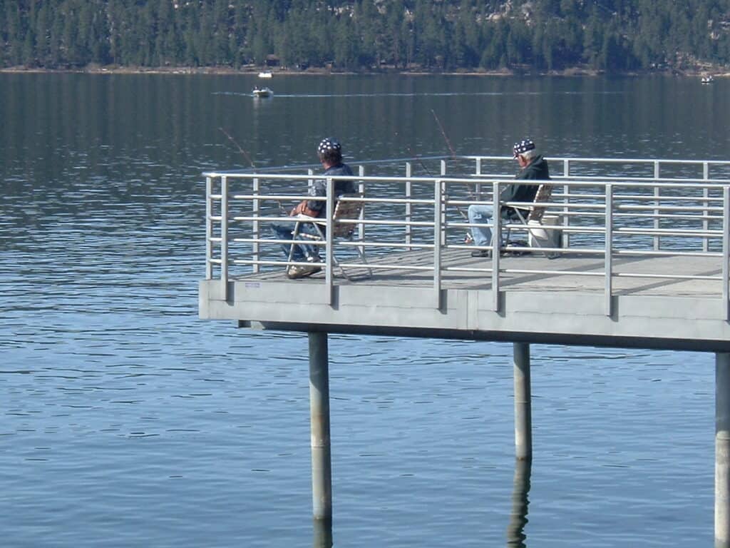 Anglers fish from a public pier while a boat in the distance motors across Big Bear Lake in Southern California's mountains.